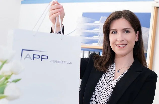 Eine Mitarbeiterin blickt freundlich in die Kamera und übergibt die APP-Tasche.