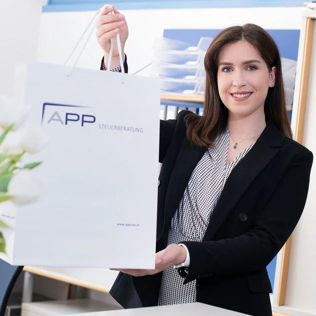 Eine Mitarbeiterin blickt freundlich in die Kamera und übergibt die APP-Tasche.