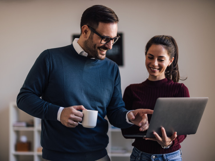 Lächelnde Kollegen, verbringen gemeinsam eine Kaffeepause und schauen in den Laptop